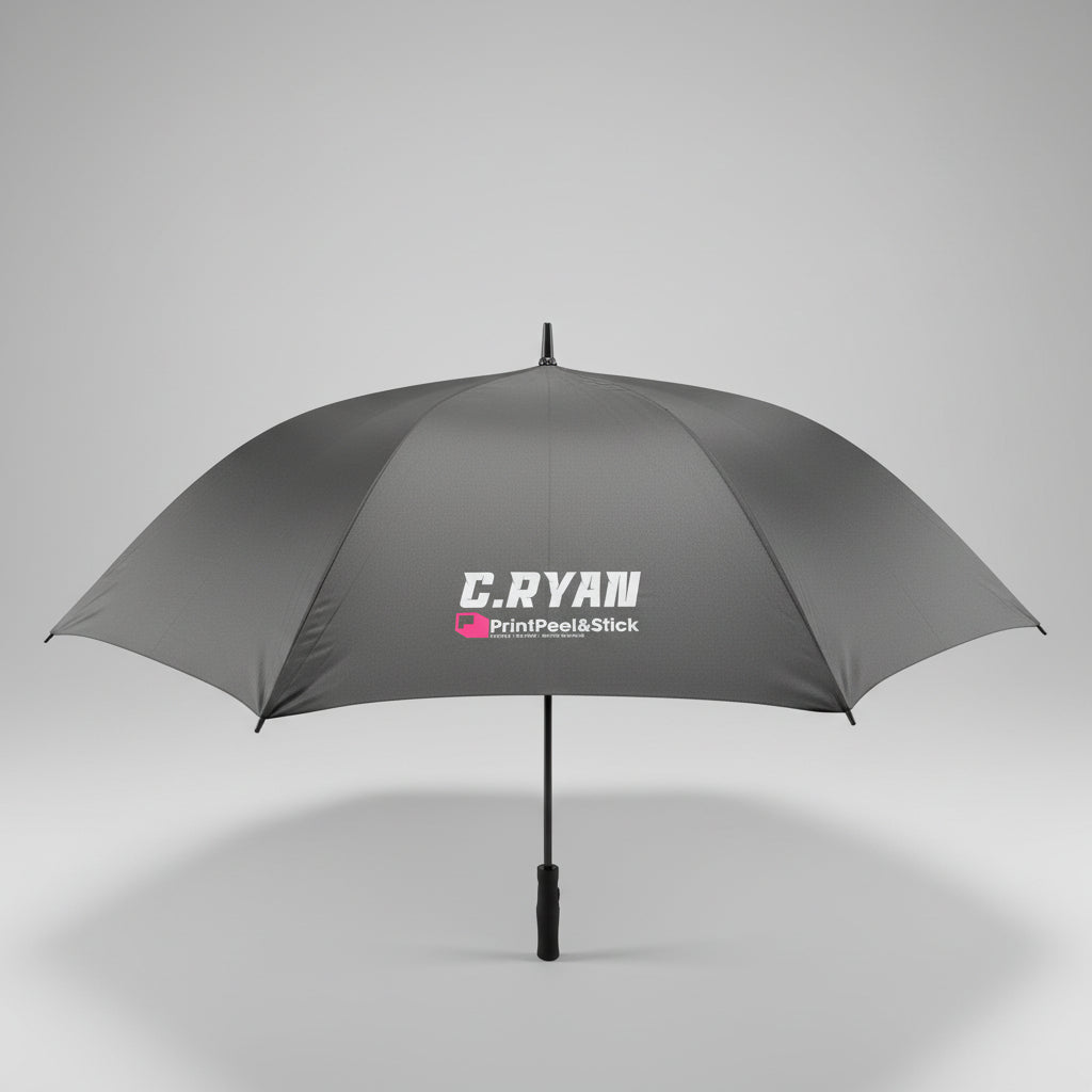A gray umbrella with a white and pink 'C.RYAM PrintPeaksStick' logo printed on the canopy, photographed on a gray carpeted floor next to a white door and office chair.