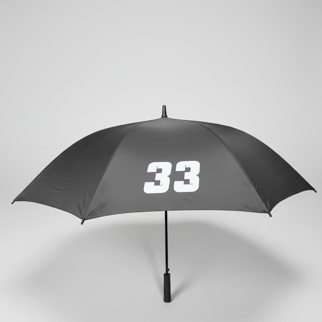 A gray umbrella with the white number 33 printed on the canopy, photographed indoors on a dark carpeted floor with office furniture partially visible at the edges.