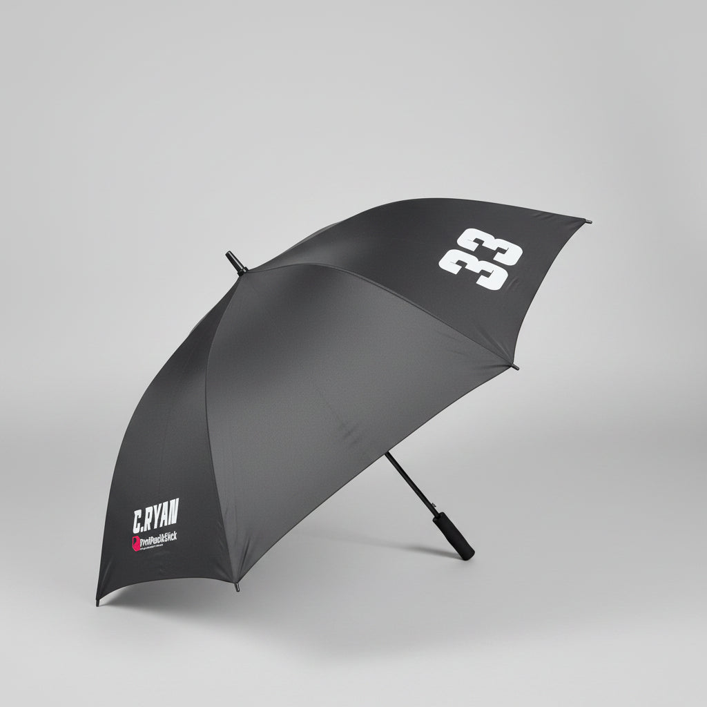 A dark gray golf umbrella with white printed logos, shown open on a gray carpeted floor in an office setting.