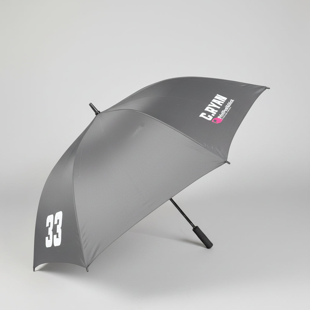 A dark gray open umbrella with white printed text reading 'C.RYAN' and a large white '33' near the lower edge, photographed indoors on a gray carpeted floor.