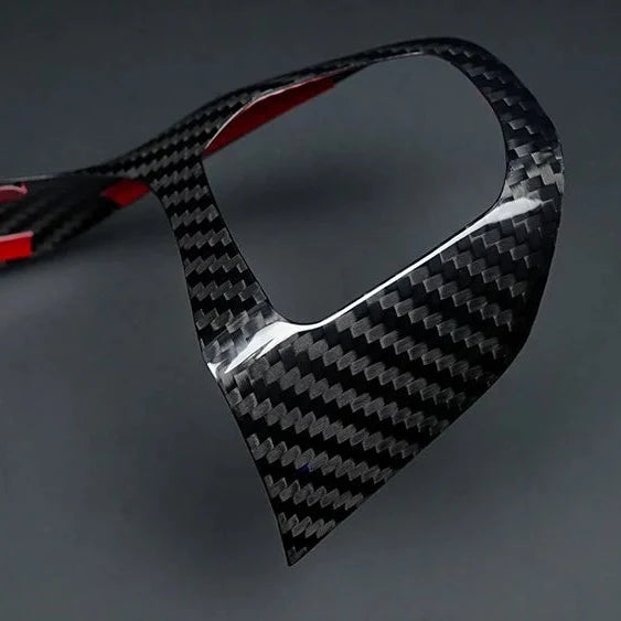 A glossy carbon fiber trim piece with a black and gray woven pattern and red inner lining, shown on a dark gray background.