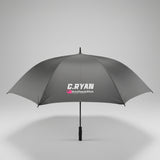 A gray umbrella with a white and pink 'C.RYAM PrintPeaksStick' logo printed on the canopy, photographed on a gray carpeted floor next to a white door and office chair.