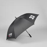 A dark gray golf umbrella with white printed logos, shown open on a gray carpeted floor in an office setting.
