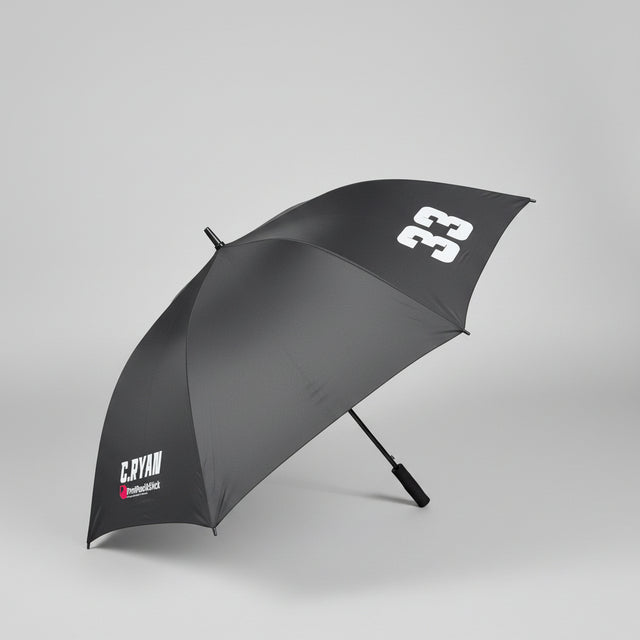 A dark gray golf umbrella with white printed logos, shown open on a gray carpeted floor in an office setting.