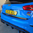 Close-up rear view of a bright blue Ford Focus ST car showing the trunk, yellow license plate, rear lights, badge, and part of the black rear diffuser.