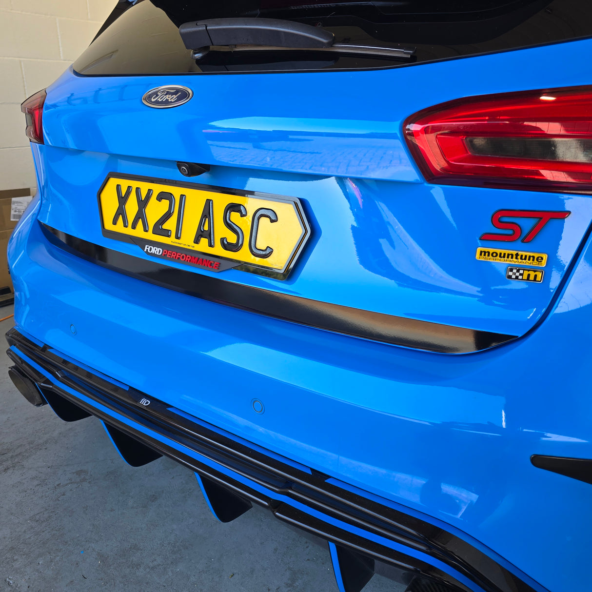 Close-up rear view of a bright blue Ford Focus ST car showing the trunk, yellow license plate, rear lights, badge, and part of the black rear diffuser.