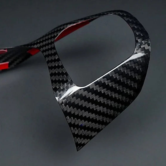 A glossy carbon fiber trim piece with a black and gray woven pattern and red inner lining, shown on a dark gray background.