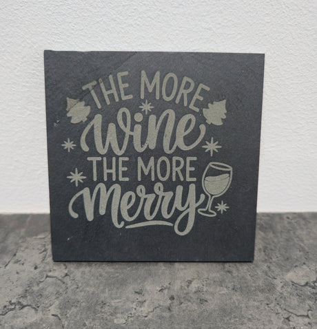 Slate coaster with 'The More Wine The More Merry' text and wine glass illustration on a gray surface.