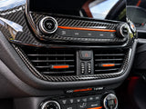 Close-up of a car dashboard with carbon fiber trim, circular control buttons, air vents, and orange accent lines. Visible text includes 'FORD PERFORMANCE 1 of 600'.