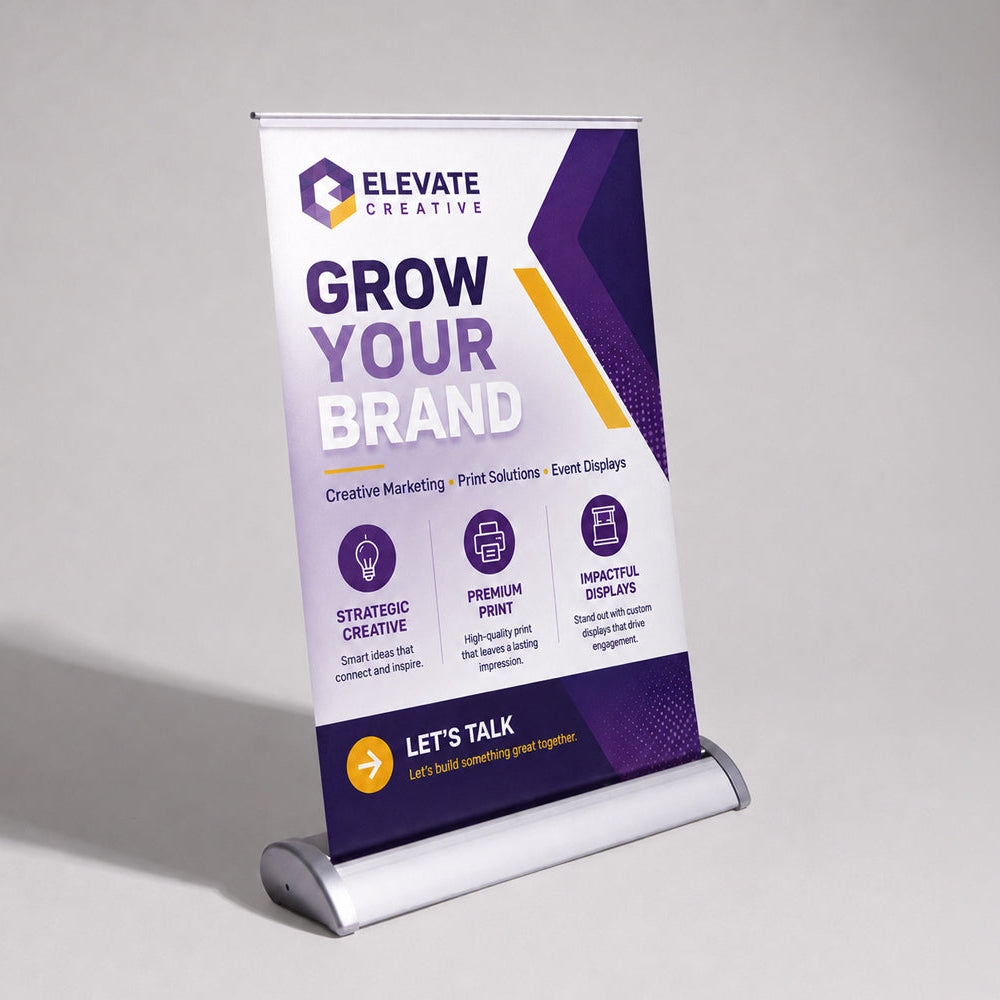 A freestanding roll-up banner stand displaying a promotional design for Elevate Creative, with the headline 'Grow Your Brand' on a white, purple, and yellow background, photographed on a light gray studio surface.