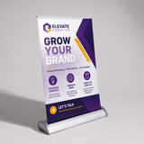 A freestanding roll-up banner stand displaying a promotional design for Elevate Creative, with the headline 'Grow Your Brand' on a white, purple, and yellow background, photographed on a light gray studio surface.