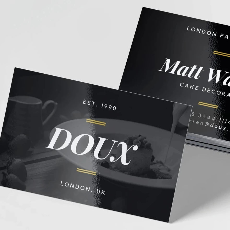 A stack of black glossy business cards with white text and gold accents, featuring the name 'Doux' and 'London UK' on the front.